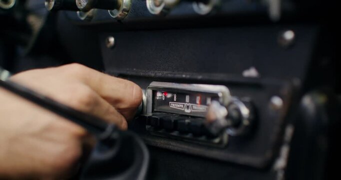 The man turns on the radio in the car, close-up of his hand as he turns the screw