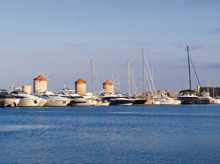 Traditional windmills overlooking Rhodes marina filled with luxury yachts in a mediterranean setting. Rhodes island, Greece