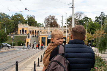 Father carrying his young son on the street near tram tracks in historic European city. Concept of parenthood, protection, urban exploration with kids and everyday family moments in the city.