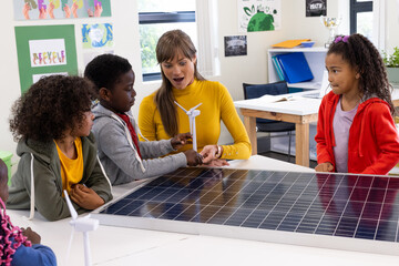 Female teacher and diverse students exploring solar energy with wind turbine in classroom, at school