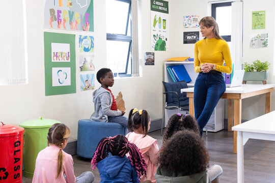 Female teacher engaging diverse students in classroom recycling lesson, kids listening, at school