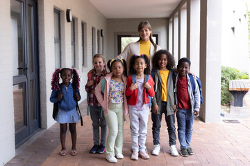 Female teacher with diverse group of smiling children standing together at school