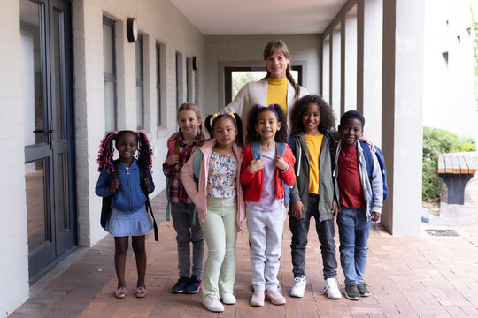 Female teacher with diverse group of smiling children standing together at school