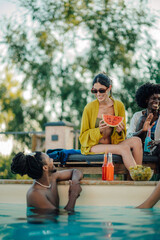 Friends enjoying watermelon and drinks by the pool during summer vacation