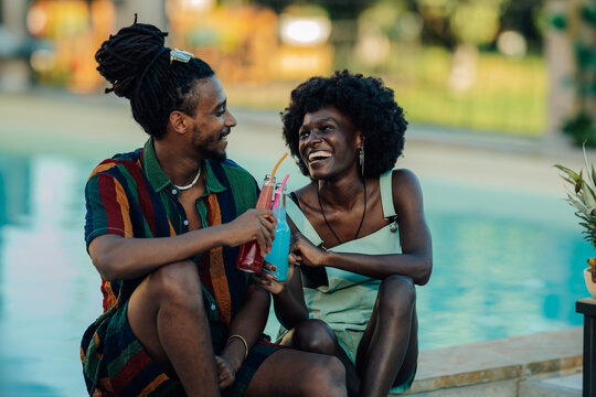 Happy couple enjoying colorful drinks by the poolside