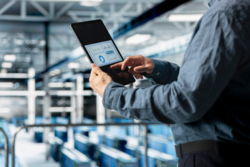 Close up of server room employee analyzing equipment metrics on device screen. Data center engineer looking at analysis charts on tablet from data gathered by infrastructure rigs