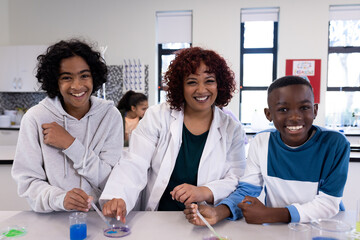 Science female teacher and diverse students experimenting with colorful liquids in school lab