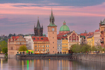 Colorful buildings and towers along the Vltava River in Prague Czech Republic at sunset with calm water and vibrant sky