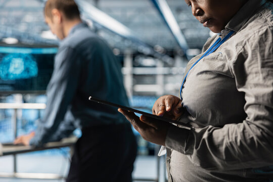 Close up of server room coworkers reviewing network configurations using software on tablet. Teamworking data center technicians tracking resource utilization trends using device