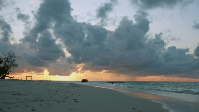 Golden sun setting over calm ocean waters near Kihaadhoo, Maldives. Peaceful shoreline and tropical silhouette.