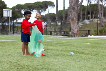 Diverse boys cleaning park, picking up plastic bottles, enjoying teamwork and nature