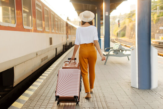 Young woman traveler with suitcase walking on railway station platform, back view, full length. Travel, active lifestyle, summer vacation