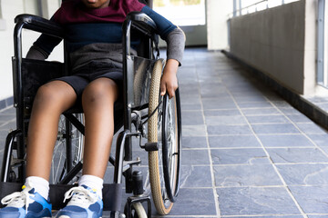 African american boy in wheelchair moving down school hallway, focusing on independence