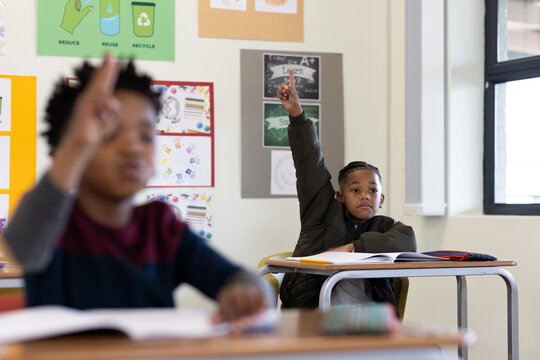 In school, young diverse boys raising hands eagerly in classroom, ready to participate