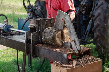 Farmer operating a tractor powered log splitter, splitting firewood logs for winter heating,...