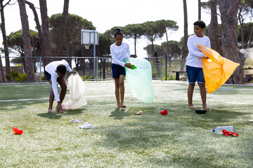 Diverse students cleaning up park, collecting litter in colorful bags, teamwork outdoors