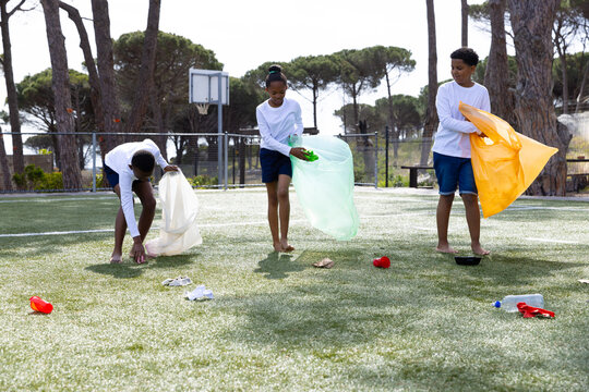 Diverse students cleaning up park, collecting litter in colorful bags, teamwork outdoors