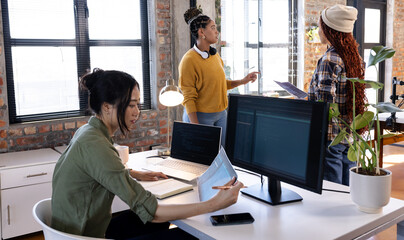 Collaborating on software, diverse women using laptops and monitors in modern office
