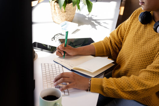 Woman coding at desk, writing notes in notebook, focused on work, at office