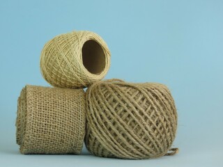 Roll of thick ecru sewing thread and roll of jute rope on blue background.