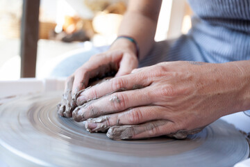 Potter’s hands shaping wet clay on spinning wheel