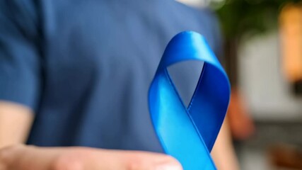 Person holds a bright blue awareness ribbon in support and solidarity for medical or social causes in an outdoor setting