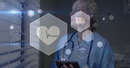 Holding tablet, scrub nurse analyzing beside blinds in corridor, with stethoscope and health icons