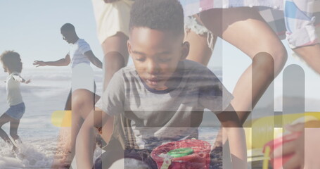 Building kneeling boy constructing sandcastle on sunny shoreline, with red bucket and green shovel