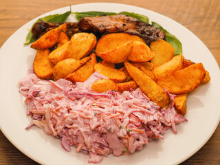 Simple meal with pork belly, potato wedges and pink coleslaw on white plate. Fine dinner with simple products.