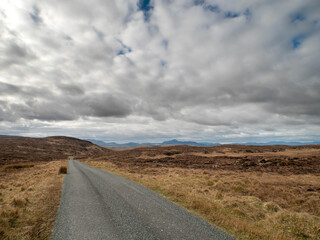 Small narrow country asphalt road leads to stunning nature background with mountains and dramatic cloudy sky. West of Ireland. Travel and tourism. Nobody.