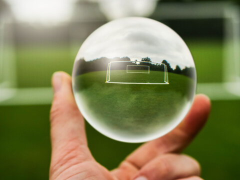 Football or soccer goal posts in glass ball which is hold by a someone hand. Forecasting sport results in popular world sport. Betting on club and national teams concept. Selective focus.