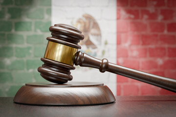 Wooden Gavel Resting on Table In Front of A Brick Wall with Mexican Flag.