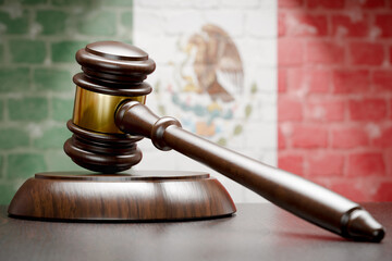 Wooden Gavel Resting on Table In Front of A Brick Wall with Mexican Flag.