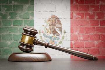 Wooden Gavel Resting on Table In Front of A Brick Wall with Mexican Flag.