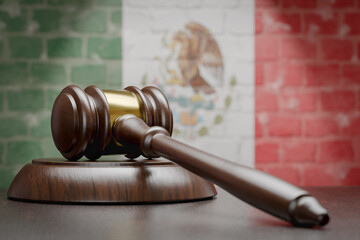 Wooden Gavel Resting on Table In Front of A Brick Wall with Mexican Flag.