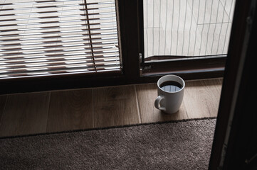 Minimalistic morning scene with a cup of black coffee on a wooden floor near a window, soft sunlight and shadows creating cozy, peaceful atmosphere and warm tones