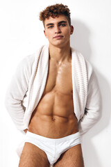 Fototapeta premium Confident young man posing in white underwear with towel wrapped around his shoulders, showcasing an athletic build. Concept of fitness and self-assurance.