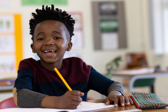 African American boy writing in open notebook at school desk with yellow pencil and plaid pouch