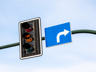 Closeup of an amber traffic light illuminated orange signal next to blue right turn road sign, urban street intersection waiting, caution, driving regulations, laws, transportation direction concept