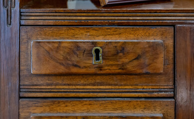 Close up front view of a vintage wooden drawer with a keyhole lock in antique furniture old cabinet texture detail aged hardwood surface background interior design asset restoration locksmith heritage