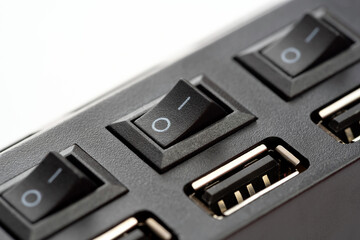 Macro closeup of an USB hub with multiple ports and power switches in off position, black plastic casing detail showing manual control for device connection and power management in tech setup, closeup
