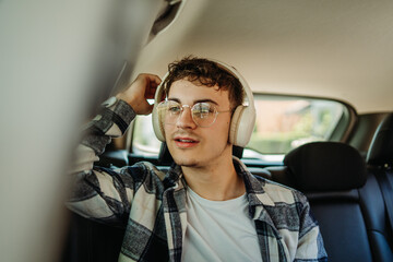 Young caucasian man student traveling on backseat in car with wireless headphones 