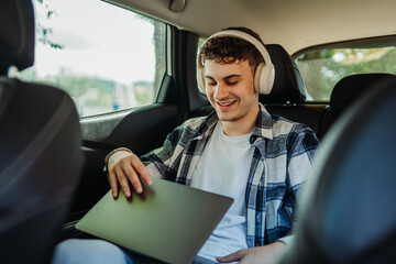 Young caucasian man student traveling and using laptop on backseat of car