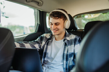 Young caucasian man student traveling and using laptop on backseat of car