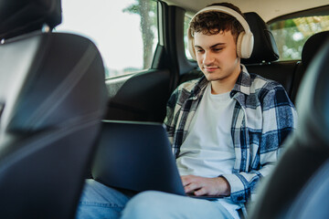 Young caucasian man student traveling and using laptop on backseat of car