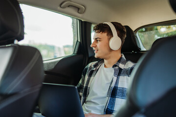 Young caucasian man student traveling and using laptop on backseat of car