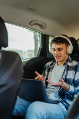 Young caucasian man student traveling and using laptop on backseat of car