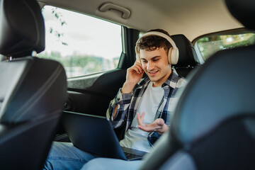 Young caucasian man student traveling and using laptop on backseat of car