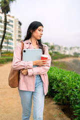 Fototapeta premium Freelancer walking in city park holding tablet and coffee