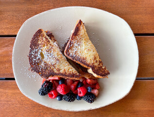 Stuffed French toast sprinkled with powder sugar and mixed berries on the side.